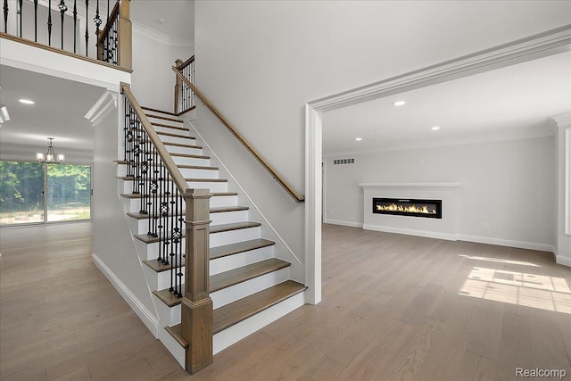 56350 Willow Creek Blvd, Utica, MI 48316 - stairs featuring ornamental molding, a glass covered fireplace, wood finished floors, a chandelier, and recessed lighting