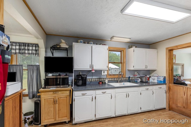 3119 S Hillman Rd, Sidney, MI 48885 - kitchen featuring stainless steel microwave, white cabinetry, light wood-style floors, dark countertops, and a textured ceiling