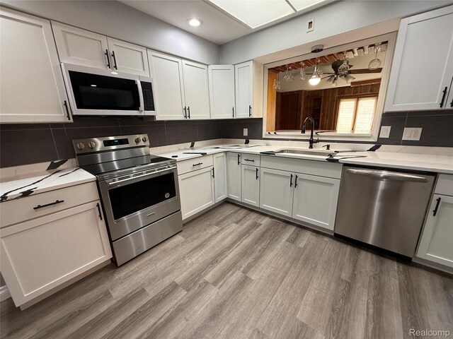 1321 Rainbow Dr, Saginaw, MI 48638 - kitchen featuring stainless steel appliances, light countertops, light wood-style floors, decorative backsplash, and white cabinets