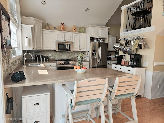 1005 W Lake St, Tawas City, MI 48763 - kitchen with appliances with stainless steel finishes, a peninsula, decorative backsplash, light wood-style floors, and a breakfast bar