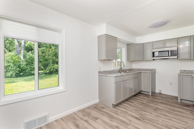 2411 Sheridan Ave, Saginaw, MI 48601 - kitchen with gray cabinets, stainless steel microwave, light wood-type flooring, and light countertops
