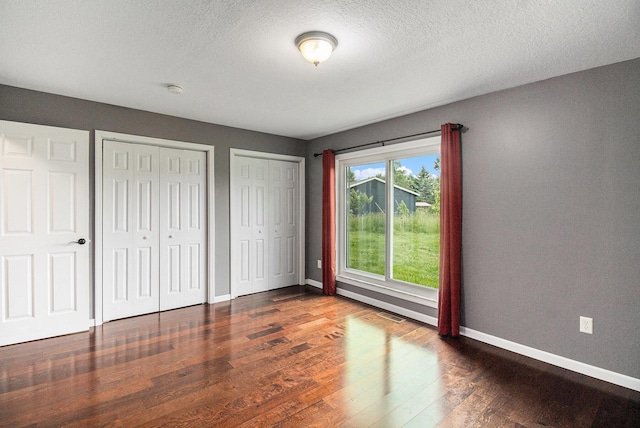 8175 Chamberlin Rd, Dexter, MI 48130 - unfurnished bedroom featuring multiple closets, dark wood-style flooring, and a textured ceiling