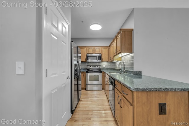 41606 Hamlet Ln, Novi, MI 48375 - kitchen featuring stainless steel appliances, light wood-style flooring, brown cabinetry, decorative backsplash, and dark stone countertops