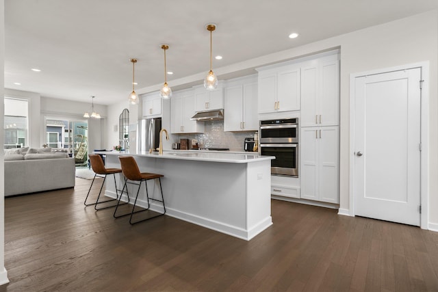 2949 Aughton Rd, Ann Arbor, MI 48105 - kitchen with appliances with stainless steel finishes, dark wood-style floors, a center island with sink, decorative backsplash, and white cabinetry