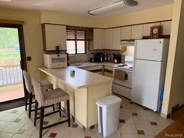 5496 Elizabeth Lake Rd, Waterford, MI 48327 - kitchen featuring white appliances, a peninsula, under cabinet range hood, light countertops, and a kitchen breakfast bar