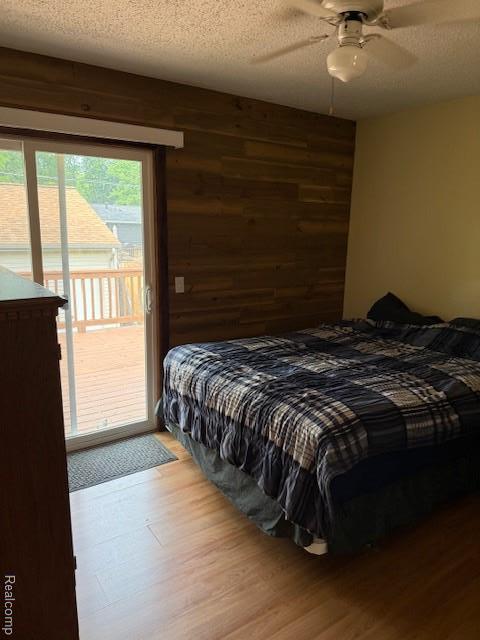 5496 Elizabeth Lake Rd, Waterford, MI 48327 - bedroom featuring access to exterior, wood finished floors, a textured ceiling, wood walls, and ceiling fan