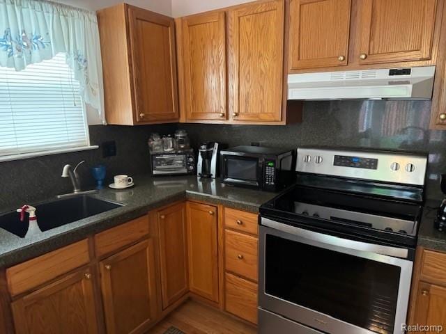 912 Rikki Anne Ct, Wixom, MI 48393 - kitchen with electric stove, under cabinet range hood, black microwave, dark countertops, and brown cabinetry