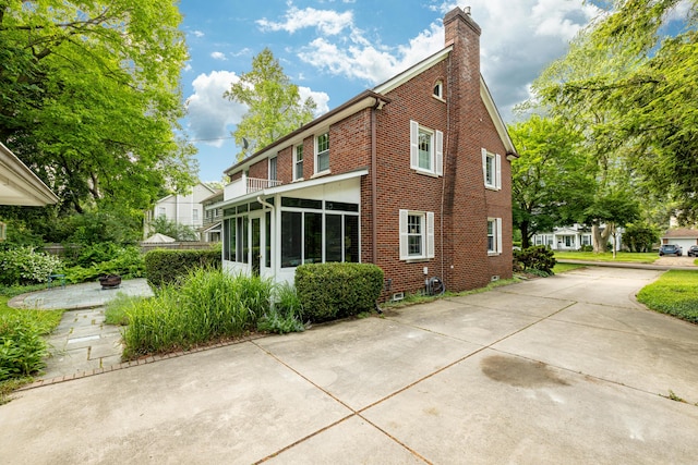 1208 Whittier Rd, Ypsilanti, MI 48197 - back of property featuring a chimney, a sunroom, concrete driveway, and brick siding