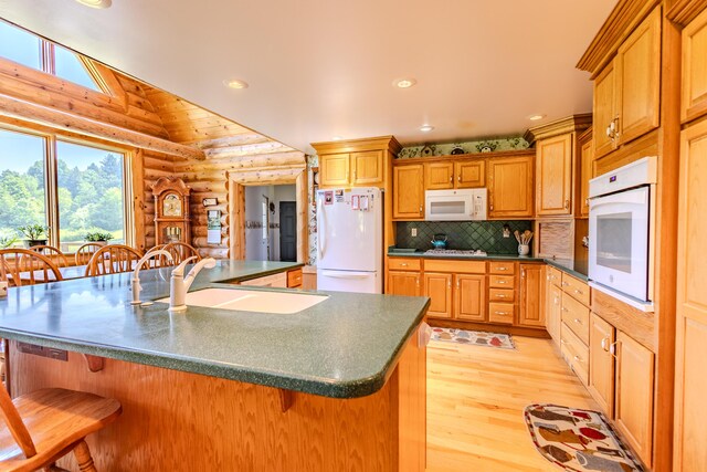 7111 Gilbert Rd, Pittsford, MI 49271 - kitchen with white appliances, rustic walls, dark countertops, light wood-type flooring, and a breakfast bar area