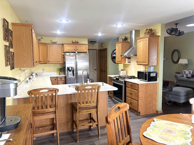 3004 Mackinaw Meadows Dr, Saginaw, MI 48603 - kitchen featuring appliances with stainless steel finishes, wall chimney exhaust hood, a peninsula, wood finished floors, and a kitchen breakfast bar