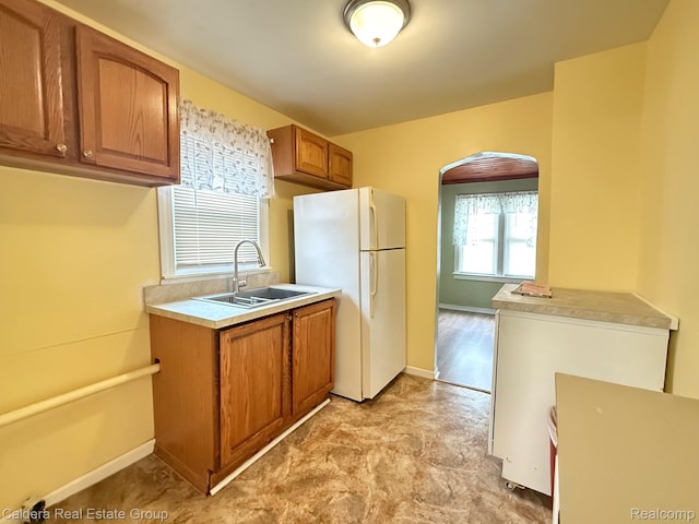 1149 E Milton Ave, Hazel Park, MI 48030 - kitchen with freestanding refrigerator, arched walkways, brown cabinetry, light countertops, and light flooring