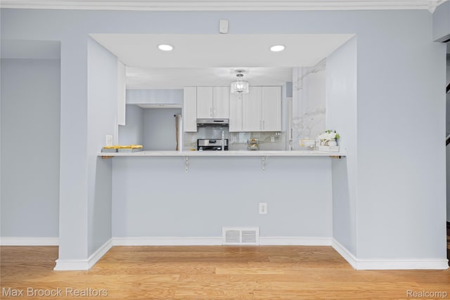 29656 Brentwood St, Southfield, MI 48076 - kitchen featuring a breakfast bar area, white cabinetry, under cabinet range hood, light wood-type flooring, and recessed lighting