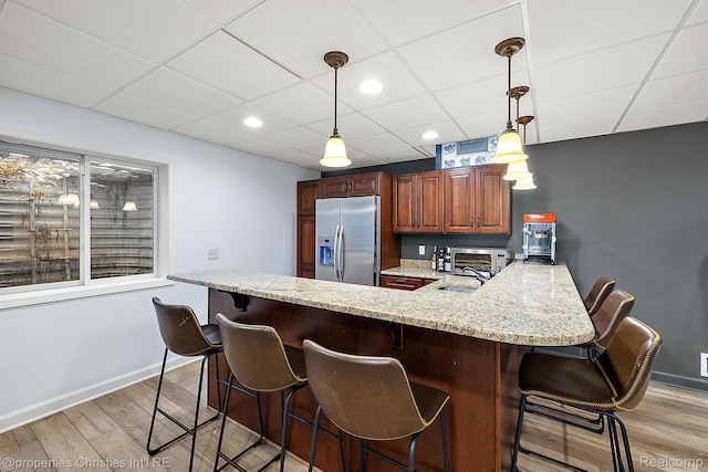 1174 Lakeside Dr, Birmingham, MI 48009 - kitchen with stainless steel fridge with ice dispenser, light wood-style floors, a kitchen bar, a peninsula, and a paneled ceiling