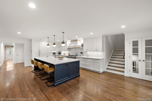 1174 Lakeside Dr, Birmingham, MI 48009 - kitchen with custom range hood, range, white cabinets, light countertops, and dark wood-style floors