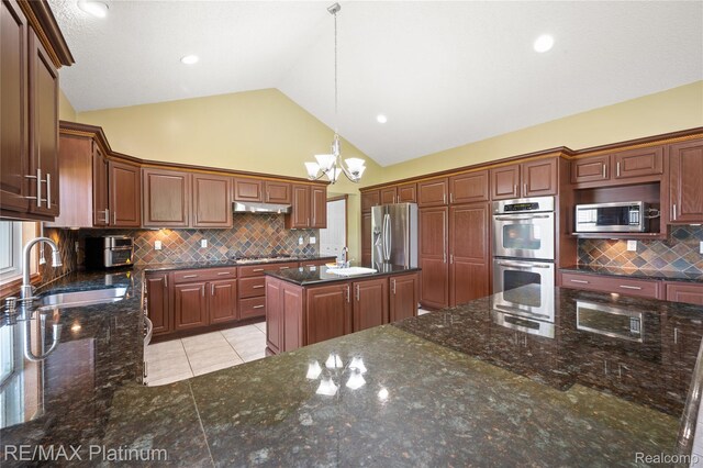 8922 Mcclements Rd, Brighton, MI 48114 - kitchen featuring appliances with stainless steel finishes, a chandelier, decorative backsplash, dark stone counters, and under cabinet range hood