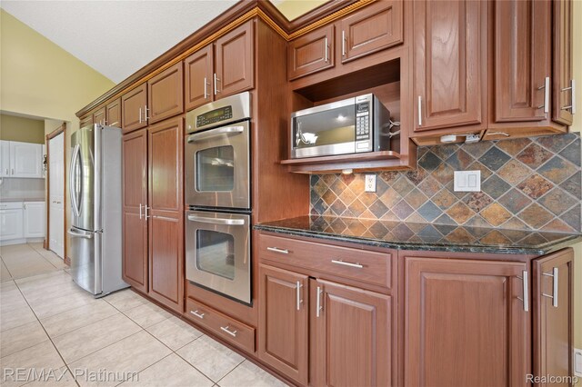 8922 Mcclements Rd, Brighton, MI 48114 - kitchen featuring stainless steel appliances, light tile patterned floors, brown cabinetry, dark stone counters, and tasteful backsplash