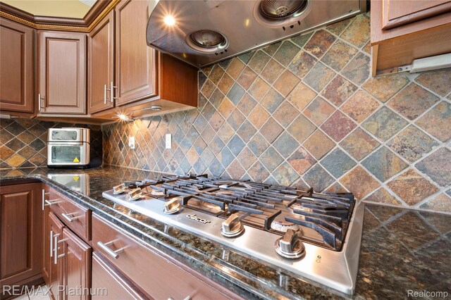 8922 Mcclements Rd, Brighton, MI 48114 - kitchen featuring ventilation hood, stainless steel gas stovetop, tasteful backsplash, dark stone counters, and brown cabinetry