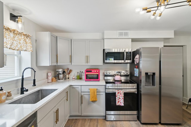 217 S Marshall Ave, Marshall, MI 49068 - kitchen with appliances with stainless steel finishes, light wood finished floors, gray cabinetry, a chandelier, and light stone counters
