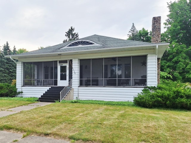 624 N Main St, Evart, MI 49631 - view of front of house with a sunroom, a chimney, a front yard, and a shingled roof