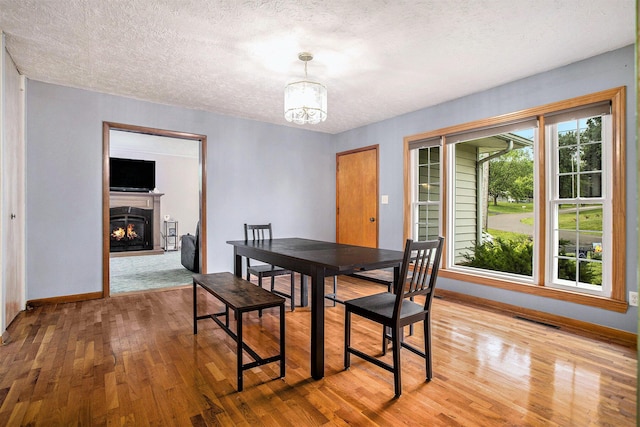 201 Beaumont Dr, Battle Creek, MI 49014 - dining room with a chandelier, light wood-style flooring, a textured ceiling, and a lit fireplace