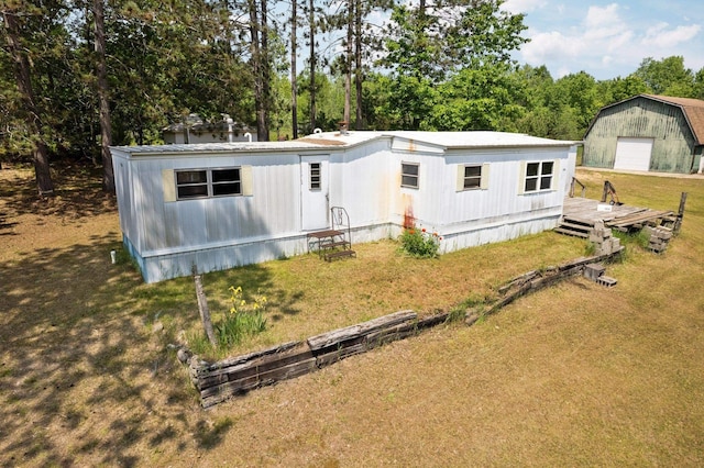 6038 SW Maple Hill Rd, Fife Lake, MI 49633 - manufactured / mobile home with a detached garage, a front lawn, an outbuilding, and view of scattered trees