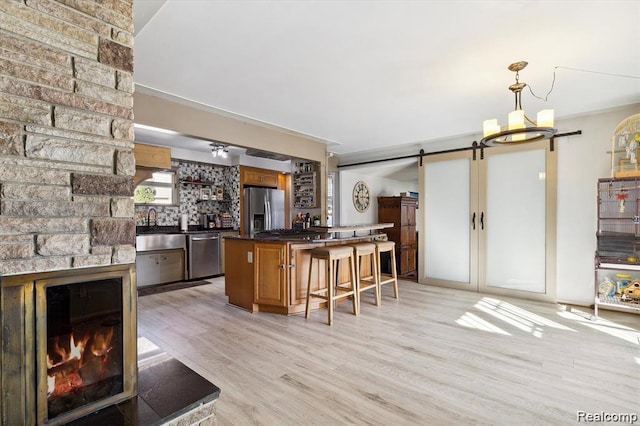 6003 Rolton Ct, Waterford, MI 48329 - kitchen featuring appliances with stainless steel finishes, a barn door, dark countertops, light wood-style floors, and a breakfast bar area