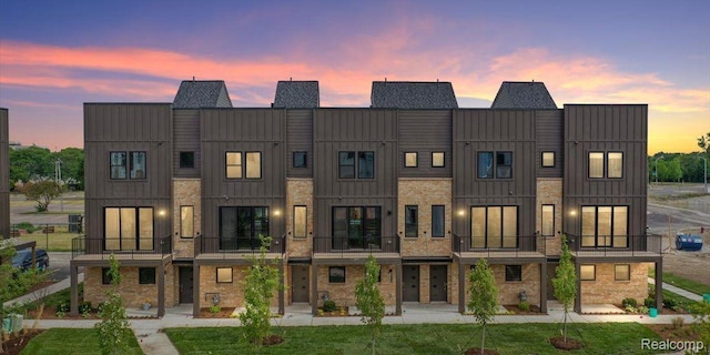 1058 Hampton Cir Unit 74, Detroit, MI 48207 - back of house at dusk featuring board and batten siding, brick siding, and a balcony