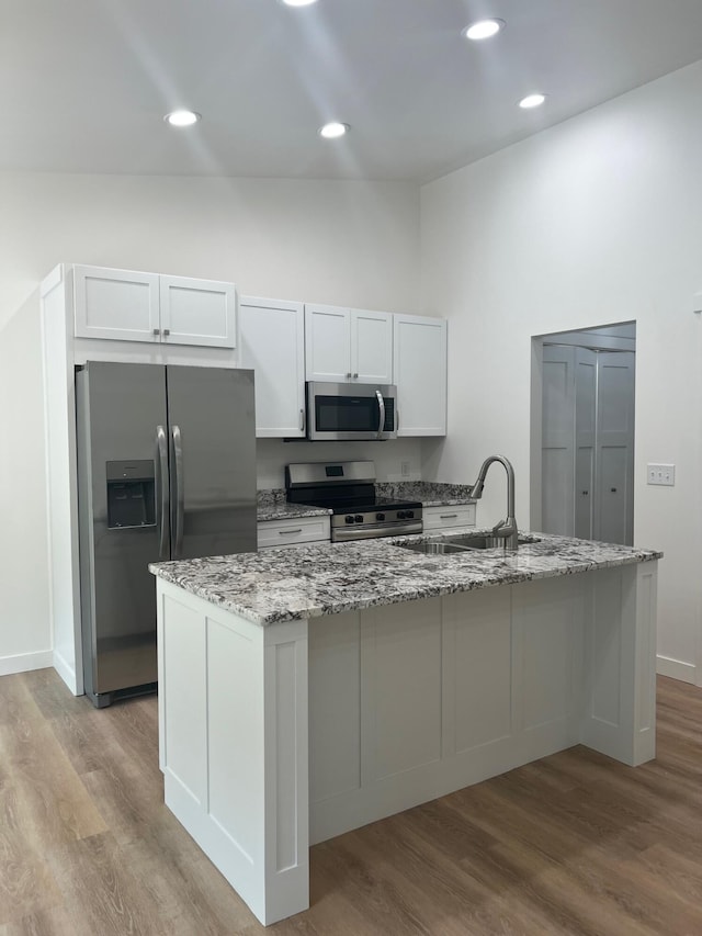 2959 Polaris Ave, Kalamazoo, MI 49004 - kitchen featuring appliances with stainless steel finishes, wood finished floors, light stone countertops, a center island with sink, and white cabinets