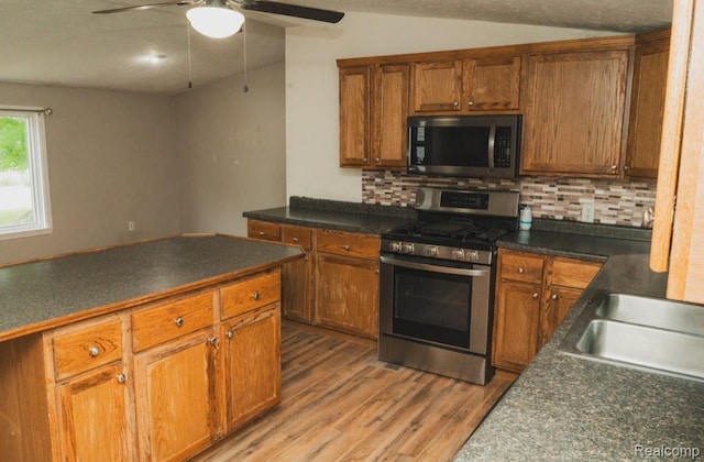 11709 Old Belding Rd NE, Belding, MI 48809 - kitchen featuring stainless steel range with gas cooktop, light wood-type flooring, decorative backsplash, brown cabinetry, and vaulted ceiling
