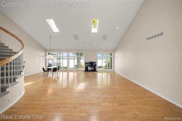 2505 Cedar Key Dr, Lake Orion, MI 48360 - unfurnished living room featuring high vaulted ceiling, stairway, light wood-style floors, a lit fireplace, and a chandelier