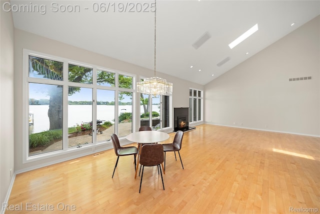 2505 Cedar Key Dr, Lake Orion, MI 48360 - dining space with high vaulted ceiling, light wood finished floors, a warm lit fireplace, a water view, and a chandelier
