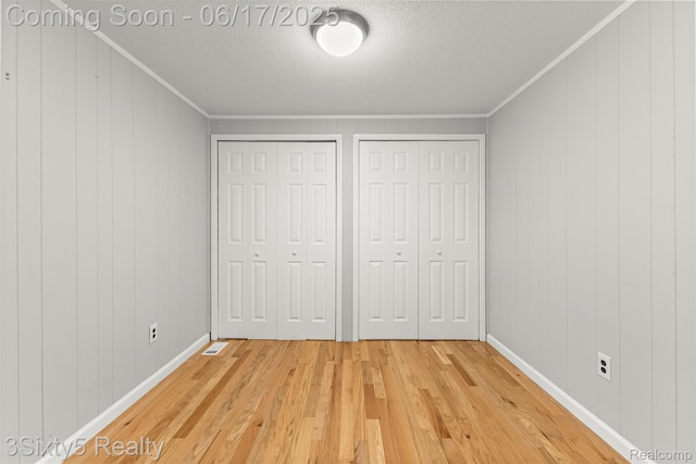 36513 Evans St, New Boston, MI 48164 - unfurnished bedroom with two closets, light wood-style floors, a textured ceiling, crown molding, and wood walls