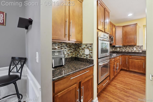 51159 Luke Ln, Novi, MI 48374 - kitchen with appliances with stainless steel finishes, light wood-style flooring, dark stone counters, decorative backsplash, and brown cabinets