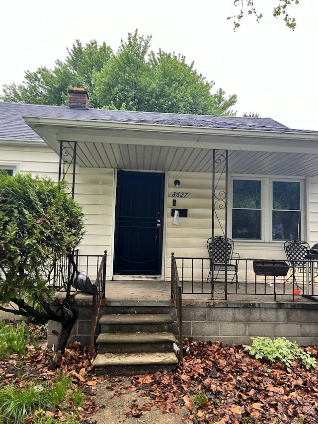 8627 Stout St, Detroit, MI 48228 - entrance to property featuring a porch, a shingled roof, and a chimney