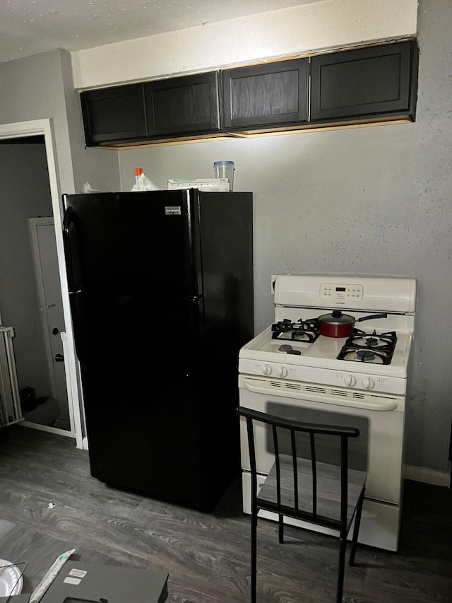 8627 Stout St, Detroit, MI 48228 - kitchen with white gas range oven, freestanding refrigerator, dark wood-style flooring, and dark cabinets