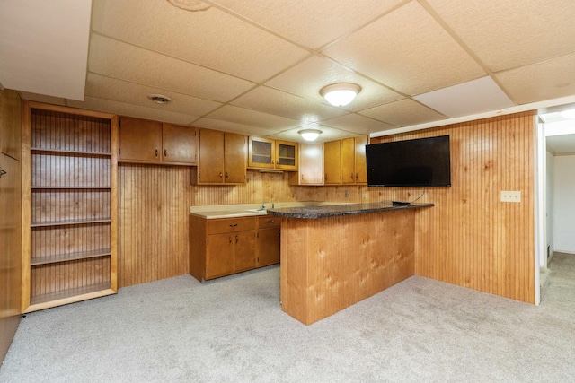 531 Gettysburg Dr, Niles, MI 49120 - kitchen featuring light carpet, brown cabinetry, a drop ceiling, wood walls, and dark countertops