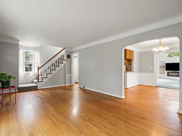 1930 Kenmore Dr, Grosse Pointe Woods, MI 48236 - unfurnished living room featuring arched walkways, stairway, light wood finished floors, and a chandelier