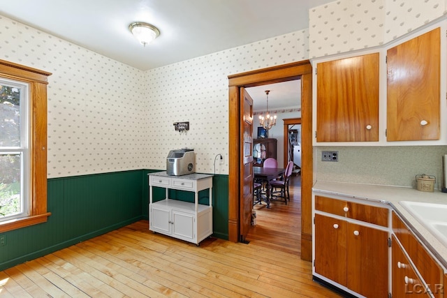 203 S Main St, Onsted, MI 49265 - kitchen featuring wallpapered walls, a chandelier, light wood finished floors, light countertops, and wainscoting