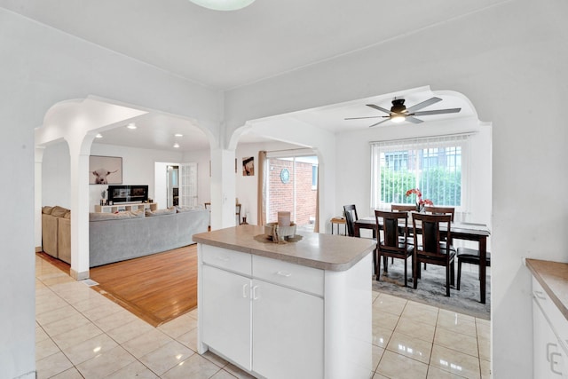 29206 Guy St, Southfield, MI 48076 - kitchen featuring light tile patterned floors, arched walkways, a ceiling fan, white cabinets, and a kitchen island