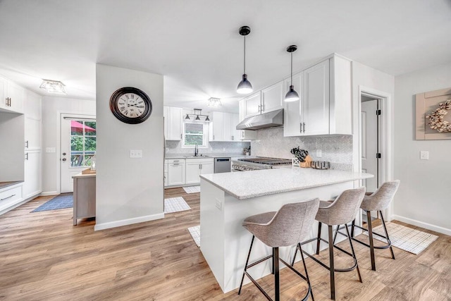 54727 Twin Lakes Rd, Dowagiac, MI 49047 - kitchen with a peninsula, under cabinet range hood, white cabinetry, backsplash, and light countertops