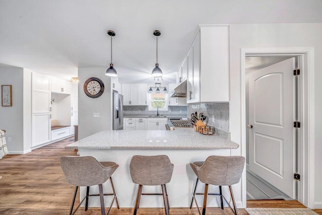 54727 Twin Lakes Rd, Dowagiac, MI 49047 - kitchen with a peninsula, under cabinet range hood, stainless steel refrigerator with ice dispenser, light stone counters, and white cabinetry