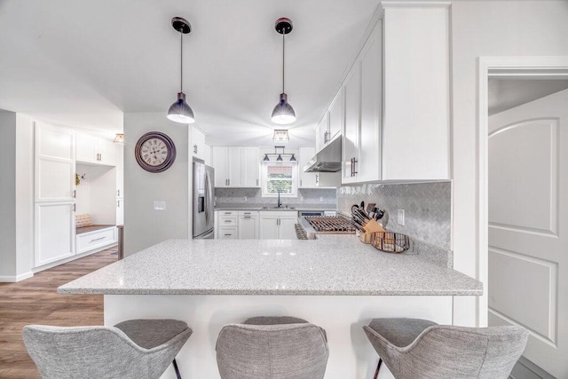54727 Twin Lakes Rd, Dowagiac, MI 49047 - kitchen featuring under cabinet range hood, stainless steel refrigerator with ice dispenser, a peninsula, decorative backsplash, and wood finished floors