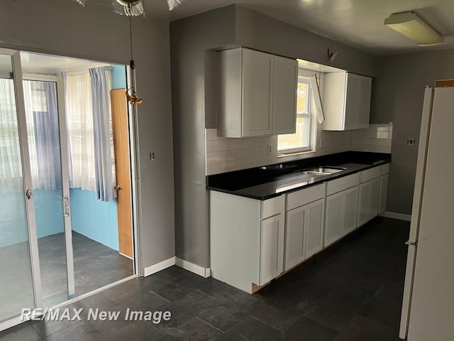 1910 Weiss St, Saginaw, MI 48602 - kitchen with freestanding refrigerator, dark countertops, tasteful backsplash, and white cabinets