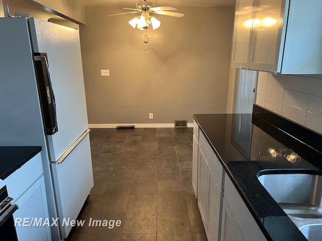 1910 Weiss St, Saginaw, MI 48602 - kitchen featuring freestanding refrigerator, a ceiling fan, tasteful backsplash, white cabinetry, and dark stone counters