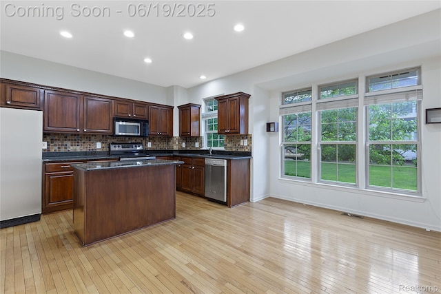 7382 Gateway Dr, West Bloomfield, MI 48322 - kitchen featuring appliances with stainless steel finishes, dark countertops, a center island, backsplash, and light wood-style flooring