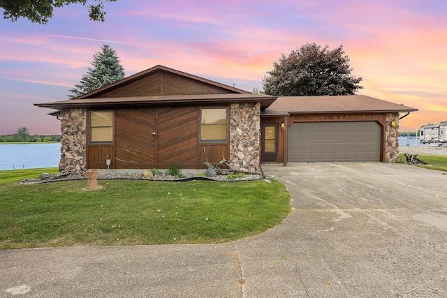 1653 Manchester Way, Gladwin, MI 48624 - view of front of house with concrete driveway, an attached garage, a lawn, stone siding, and a water view