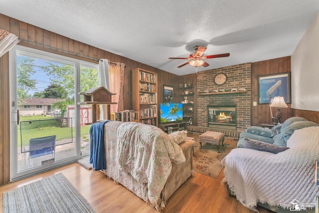 234 Crampton Dr, Monroe, MI 48162 - living room featuring wood walls, a textured ceiling, ceiling fan, wood finished floors, and a brick fireplace