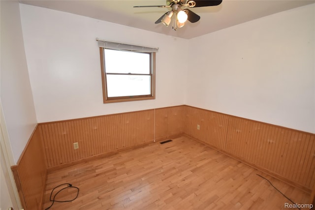 11057 Hogan Rd, Fenton, MI 48436 - unfurnished room with wainscoting, light wood-style flooring, a ceiling fan, and wooden walls