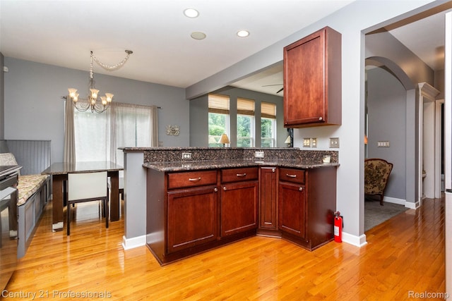 23640 Woodside Ct, South Lyon, MI 48178 - kitchen with a peninsula, light wood-type flooring, arched walkways, a chandelier, and dark stone counters