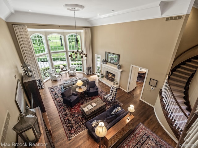 living area with a warm lit fireplace, stairway, wood finished floors, and ornamental molding